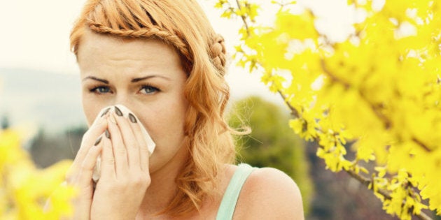 Young woman sneezing among flowers outdoors