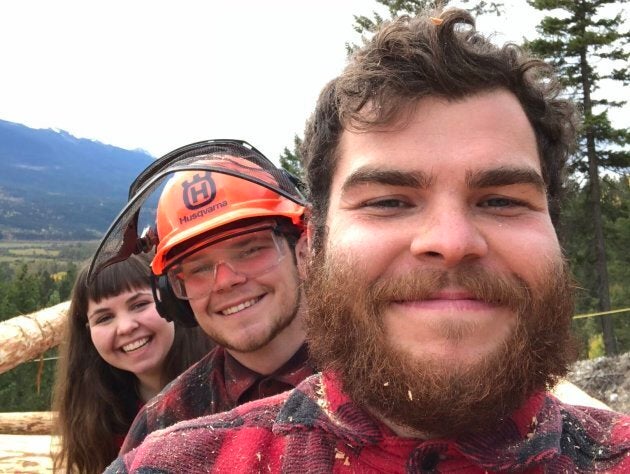 Siblings Andrew (r), Cameron, and Emily (l) pose for a photo on the build site of their family cabin.