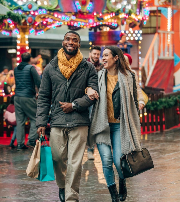 Front view of a happy couple walking along a city street. Behind them is a fun fair ride. The couple are carrying shopping bags.