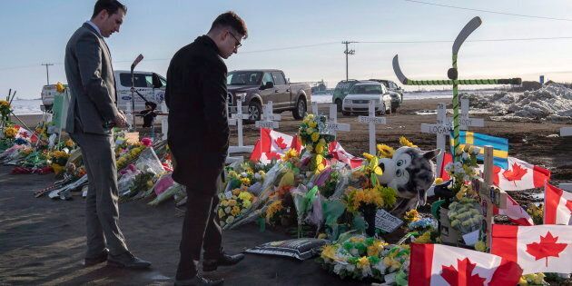 A group of Saskatchewan Junior Hockey League referees look at a memorial at the intersection of a fatal bus crash that killed 16 members of the Humboldt Broncos hockey team near Tisdale, Sask. on April 14, 2018.