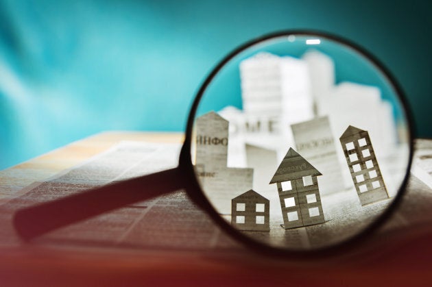 Magnifying glass in front of an open newspaper with paper houses. Concept of rent, search, purchase real estate.