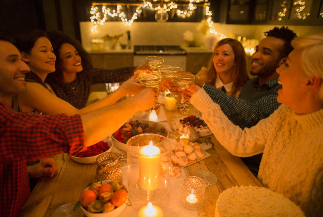 Friends toasting champagne glasses at candlelight table is hygge to the max.