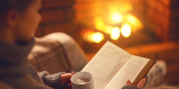 All the elements of hygge encapsulated: blanket, fireplace, tea, book and warm lighting.