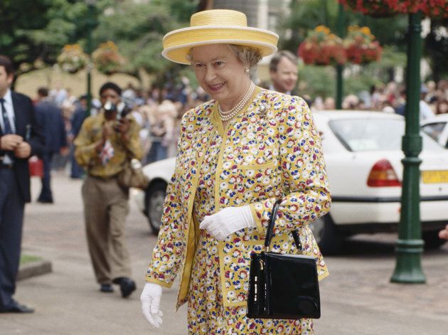 Queen Elizabeth II in Durban during a state visit to South Africa on March 25, 1995. She's wearing a rare pattern, but her hat, gloves and pearls and standard, and she's carrying the same black Launer handbag she's had since at least the 1970s.