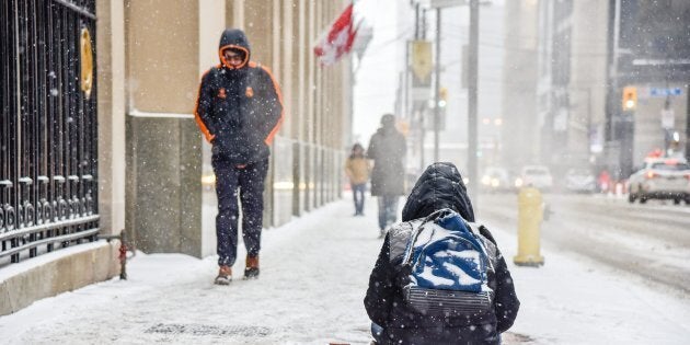 A homeless person tries to stay warm by an underground exhaust vent while trying to collect change from a passing pedestrian on Bay Street in Toronto on Jan. 19, 2019.