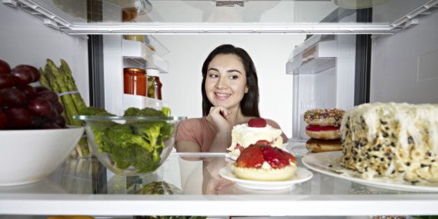 Woman looking at cake in through the fridge.