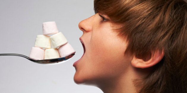 Boy poised to eat spoonful of marshmallows, which some people use to heal a sore throat.