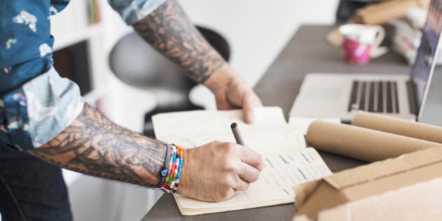 Midsection of male architect writing in book at table