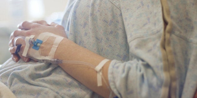 A pregnant woman in the early stages of labor rests in a hospital bed with her arms on her stomach. An IV is seen in her left hand.