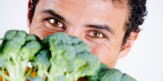 Portrait of a young man holding broccoli in front of his face