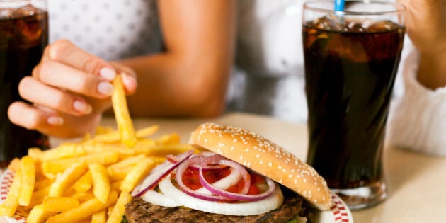 Two women - one is African American - eating hamburger and drinking soda in a fast food diner; focus on the meal