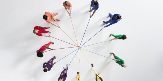 Overhead shot of a small group of people, wearing monochromatic colors, pulling at ropes from opposing directions