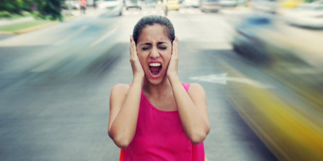 Portrait of woman standing still in the middle of a street with cars passing by fast, screaming stressed and frustrated