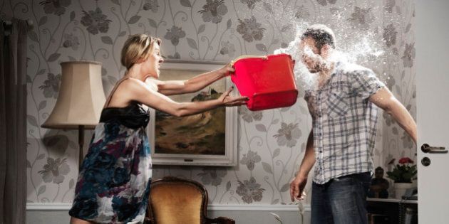 young woman thowing a bucket of water at her partner, in the living room
