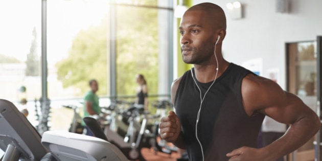 Man in a gym running on a treadmill with head phones in.