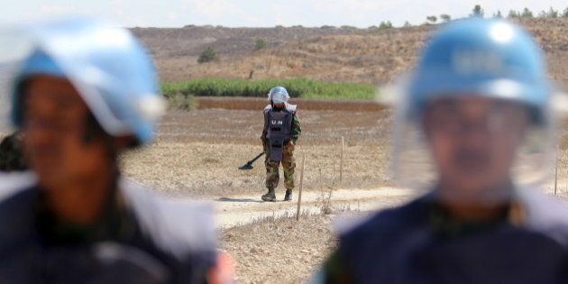 A UN mine disposal expert from Cambodia walks while holding a mine detector during a media tour in the UN-controlled buffer zone near the village of Mammari, Cyprus August 26, 2015. REUTERS/Yiannis Kourtoglou