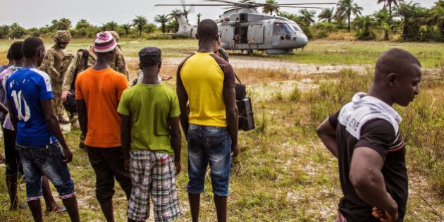 Local residents look at a British Navy helicopter after it made a food drop on Sherbro Island, Sierra Leone, Sunday, Dec. 7, 2014. The WFP, World Food Program and British Military took part in a three day food distribution effort for local residents on the remote Sherbro Island, where the Ebola virus has prevented people from farming, fishing or gathering food. (AP Photo/Michael Duff)