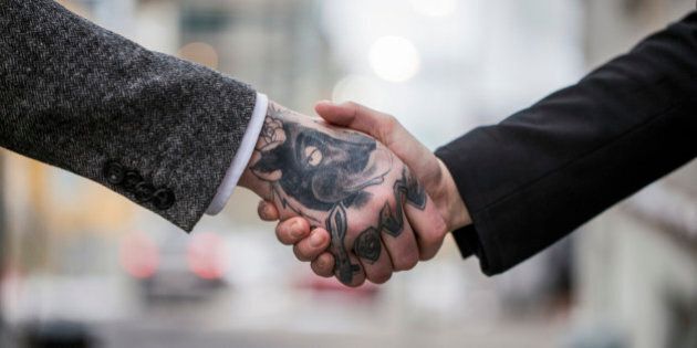 A cropped photo of business colleagues shaking hands outdoors. Tattooed businessman greeting female colleague. Male executive is with animal and text tattoo on hand.