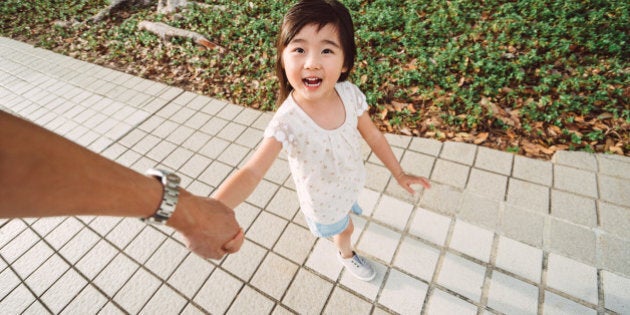 First person view of dad holding lovely little daughter's hand strolling on the street while talking to each other.