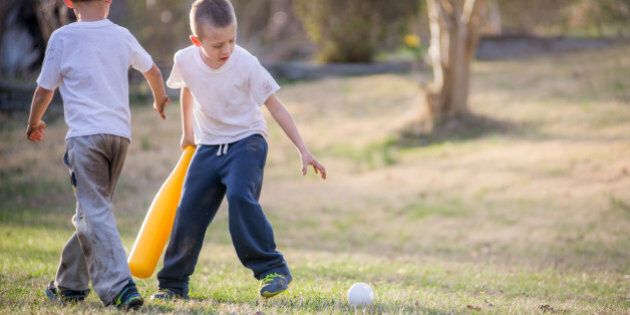 Young boys wearing dirty sweatpants and plain shirt holding a yellow bat in the front yard.