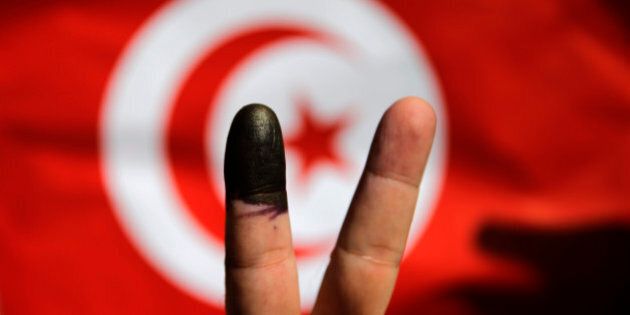 A Tunisian man shows his ink-stained finger in front of a Tunisian flag after voting for the country's parliamentary elections outside the Tunisian embassy in Cairo, Egypt, Saturday, Oct. 25, 2014. On Sunday, Tunisians will vote for their first five-year parliament since they overthrew dictator Zine El Abidine Ben Ali, marking the end of the democratic transition that they alone among the pro-democracy Arab Spring uprisings have managed to achieve. Now, many Tunisians are expressing disillusionment over democracy. (AP Photo/Hassan Ammar)