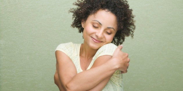 Pretty woman with curly hair hugging herself, on green background.