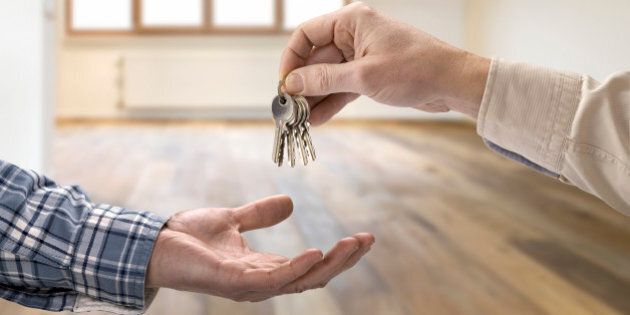 Realtor giving house key to buyer in empty room.