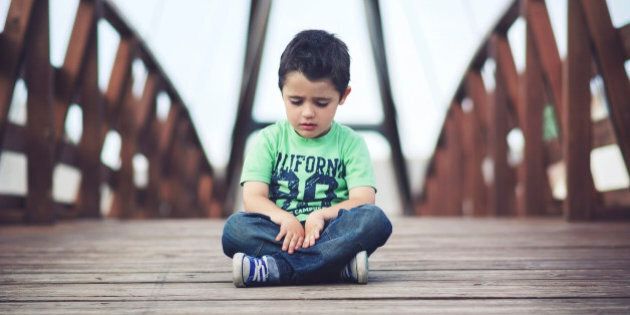 Sad and thoughtful boy sitting on a wooden bridge.