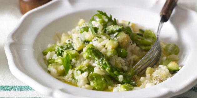 Risotto primavera served in white bowl with fork on table, close-up