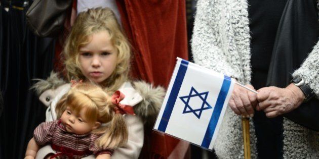 A young girl with her doll stands past a woman holding an Israeli flag and a Spanish flag during a rally in support of Israel called by Federation of Jewish Communities in Spain (FCJE) and the Jewish Community of Madrid, in front of the Israeli embassy in Madrid on October 18, 2015. Israel pressed ahead with major security measures after five more stabbing incidents, while ultra-Orthodox Jews illegally visiting a West Bank holy site set ablaze last week were assaulted by Palestinians. AFP PHOTO/ PEDRO ARMESTRE (Photo credit should read PEDRO ARMESTRE/AFP/Getty Images)