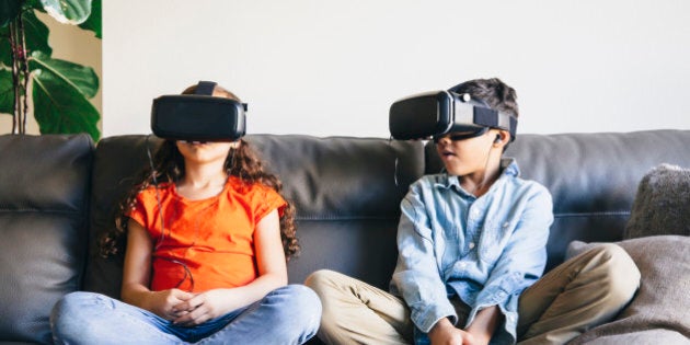 Mixed race children using virtual reality goggles on sofa