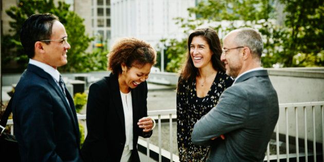 Four laughing business colleagues in discussion outside of office building