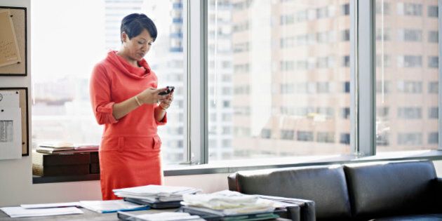 Businesswoman standing in office looking at smart phone smiling