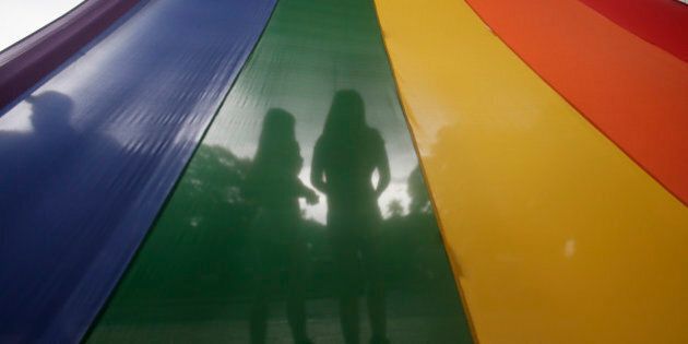 A LGBT (Lesbians Gays Bisexuals and Transgenders) couple is silhouetted by their rainbow-colored symbol while waiting to march around the University of the Philippines campus in an annual event to draw the attention to their issues as gay rights and anti-discrimination Friday, Sept. 11, 2015 at suburban Quezon city northeast of Manila, Philippines. More than a hundred LGBTs joined the march which culminated in a concert.(AP Photo/Bullit Marquez)