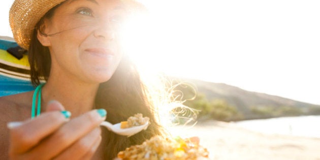 A beautiful woman with a straw hat eating a papaya with fresh granola and yogurt.