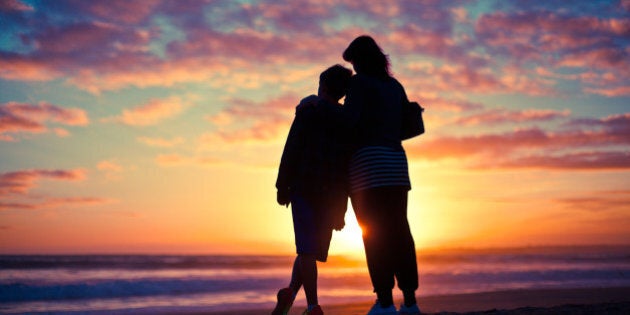 Mother and son silhouetted watching the sunset on a beach.