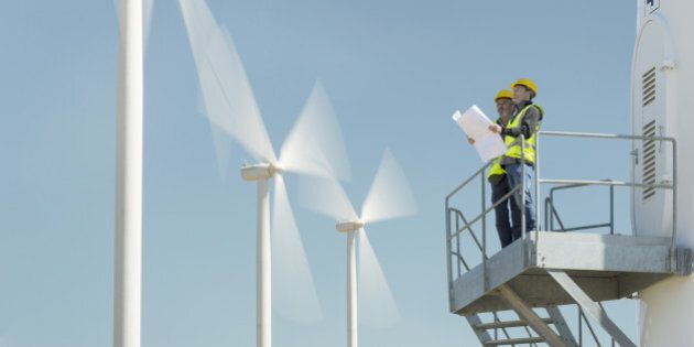 Workers standing on wind turbine in rural landscape