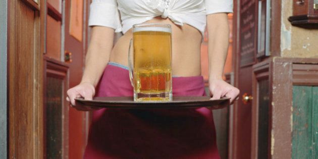 Young waitress holding glass of beer on tray, mid section