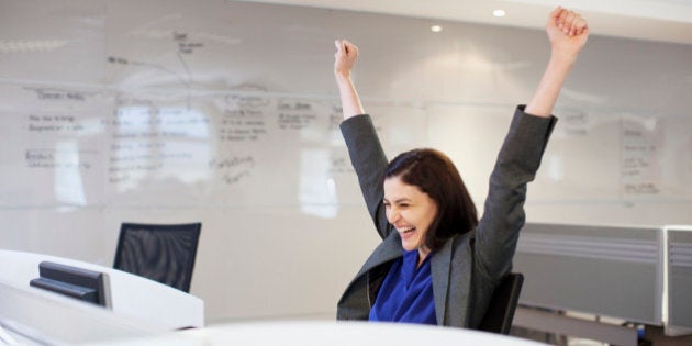 Enthusiastic businesswoman with arms raised in office