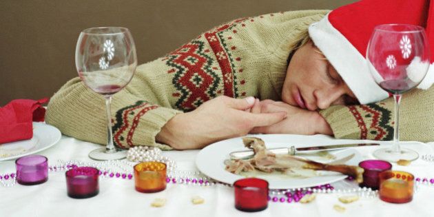 Young man in Santa hat sleeping at dinner table, resting head on arm