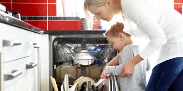 Young mother and her son loading a dishwasher in the kitchen