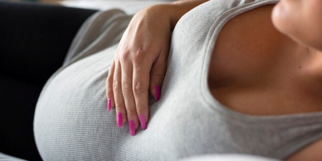 Beautiful pregnant woman relaxing and lying on the side on the bed. Holding a hand on the tummy.