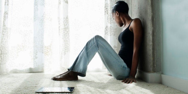 Young woman on floor next to ipad looking sad.