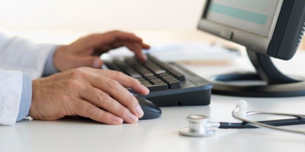 Male doctor's hands typing on desktop computer keyboard with stethoscope