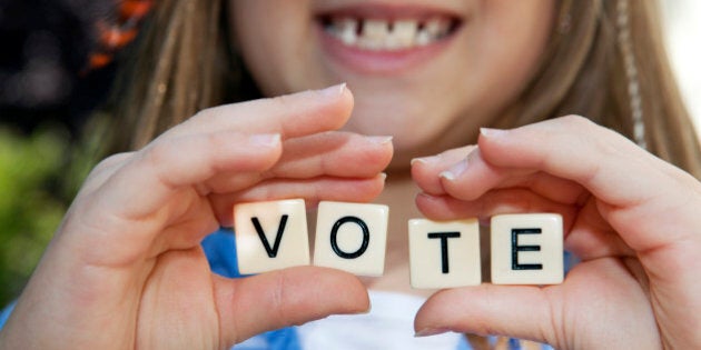 Young girl holding small block letters with message: Vote