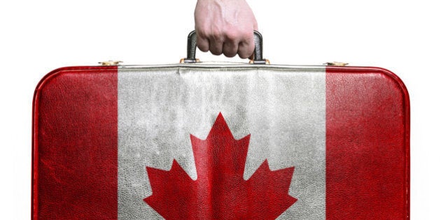 Tourist hand holding vintage leather travel bag with flag of Canada