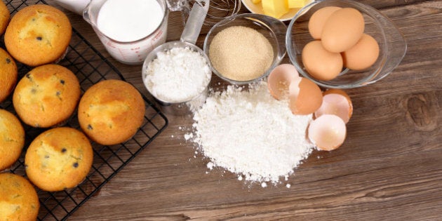 Freshly baked muffins on a dark wood table with various ingredients.