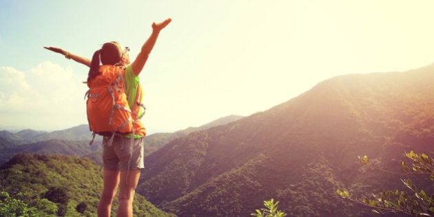 cheering woman hiker open arms at mountain peak cliff