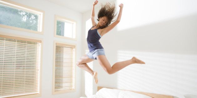 Attractive Young Woman Jumping Energetically on Bed
