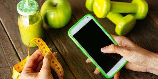 Fitness diet nutrition and workout routine smartphone app concept. Healthy green detox, apple and dumbbells for slimming down dieting. Female checking weight loss with measuring tape.